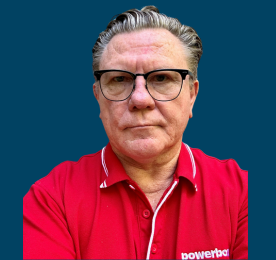 A man with glasses wearing a red company shirt in front of a solid blue backdrop.