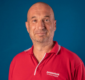 Bald man in a red uniform posing in front of a blue backdrop.