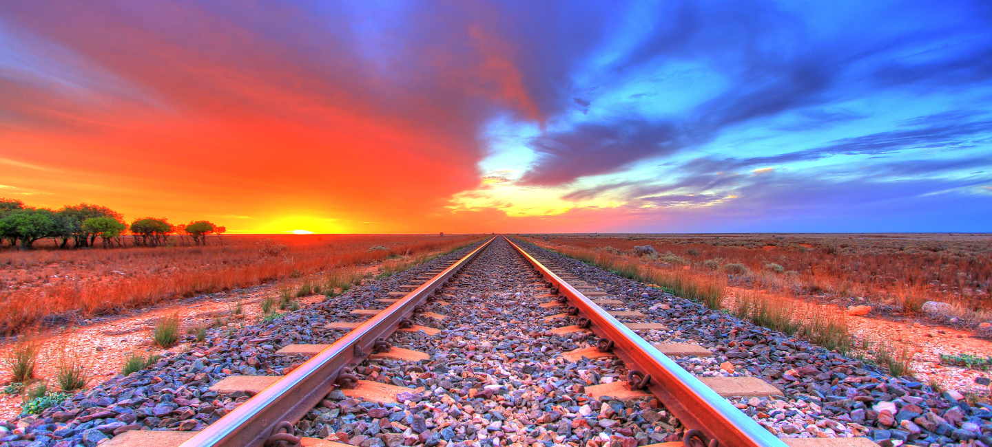 Railway tracks stretch across the outback towards the setting sun.