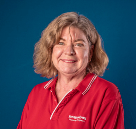 A woman with wavy hair in a red collared shirt posing against a blue background.