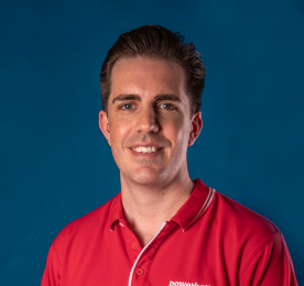 A smiling man wearing a red collared shirt posing against a blue background.
