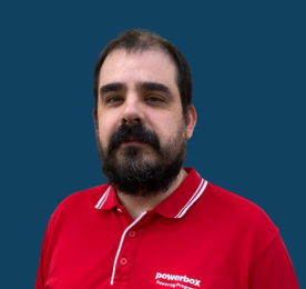 A bearded man in a red collared shirt with a blue backdrop.