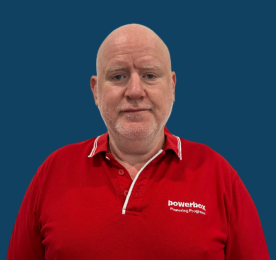 A bald man in a red company shirt standing against a plain blue background.