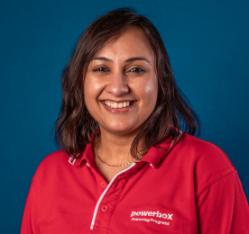 A woman smiling in a red company shirt, posed in front of a blue backdrop.