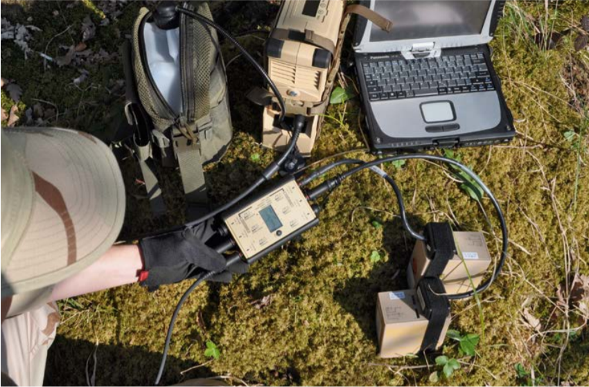 Field technician working with electronic equipment and a laptop on the grass.