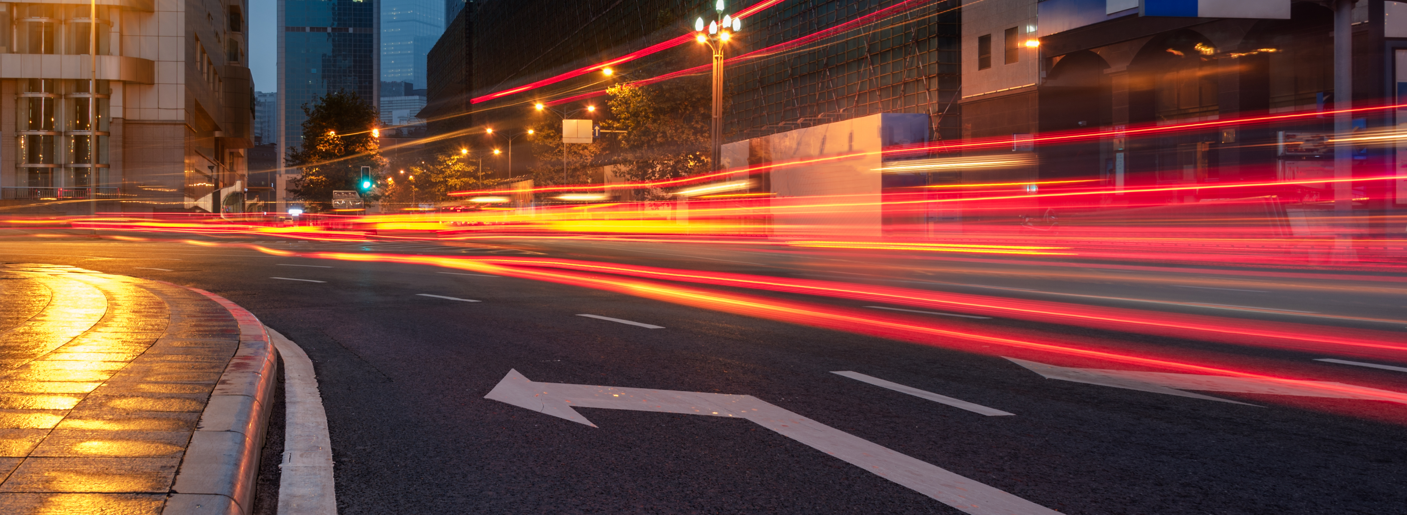 Night-time city street scene with light trails from vehicles indicating motion and urban activity.