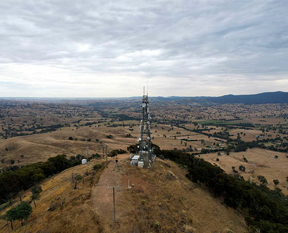 A telecommunications tower on a hilltop overlooking a vast rural landscape under a cloudy sky.