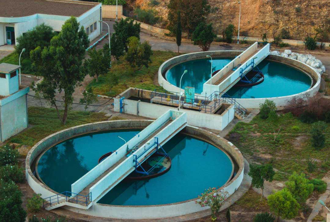 Aerial view of two large water treatment tanks surrounded by greenery and buildings.